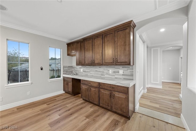 kitchen featuring tasteful backsplash, arched walkways, light countertops, crown molding, and light wood-style floors