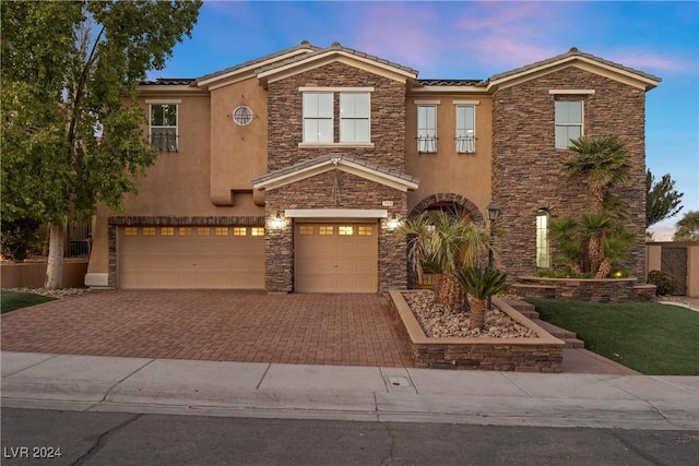 view of front of property featuring an attached garage, stone siding, decorative driveway, and stucco siding