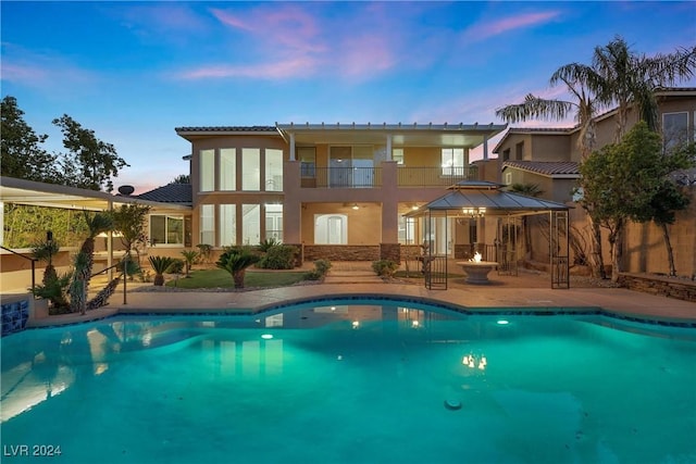 rear view of house featuring an outdoor pool, a balcony, a gazebo, a patio area, and stucco siding