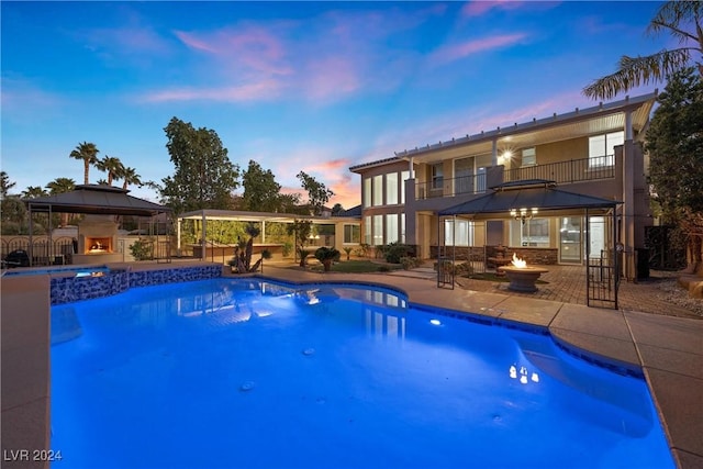 view of pool featuring a fire pit, an outdoor stone fireplace, a patio area, and a pool with connected hot tub