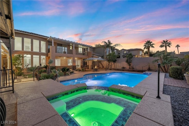 pool at dusk with an in ground hot tub and a patio area