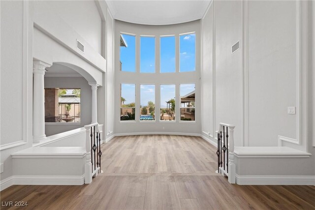 entrance foyer with decorative columns, crown molding, a towering ceiling, and light hardwood / wood-style flooring