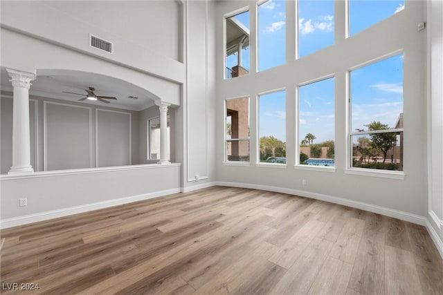 unfurnished living room with light wood-type flooring, ornate columns, ornamental molding, ceiling fan, and a high ceiling