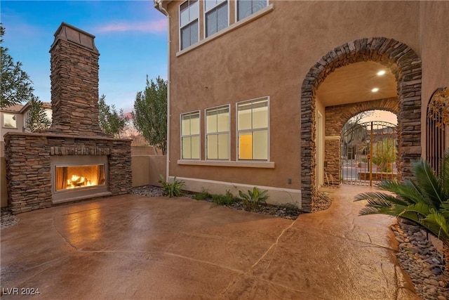 view of home's exterior featuring an outdoor stone fireplace, fence, stone siding, stucco siding, and a patio area