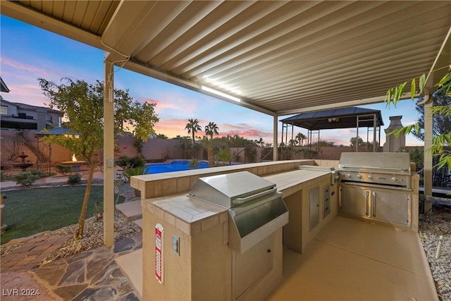 patio terrace at dusk featuring a gazebo, area for grilling, and exterior kitchen