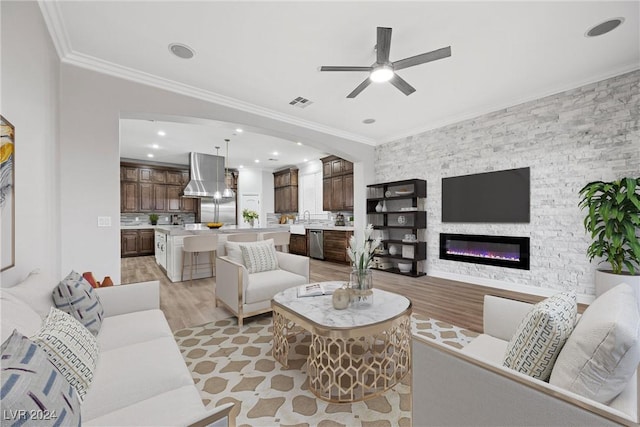 living room with light wood-style flooring, visible vents, ornamental molding, and a glass covered fireplace