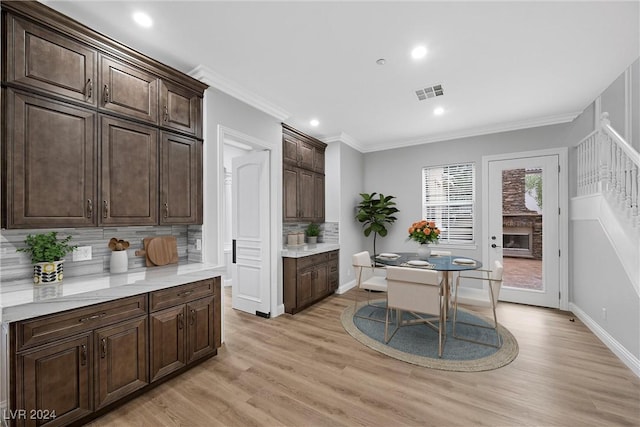 kitchen with dark brown cabinetry, tasteful backsplash, visible vents, ornamental molding, and light wood-style floors