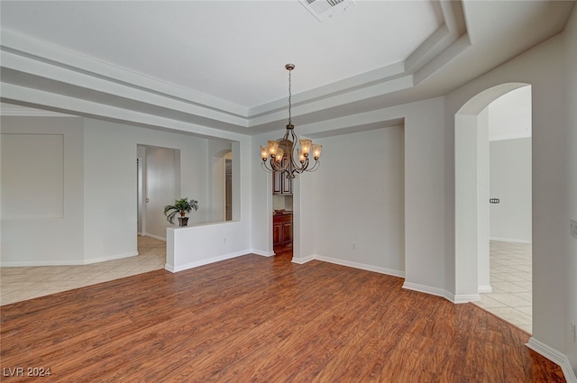 unfurnished room featuring light hardwood / wood-style floors, an inviting chandelier, and a raised ceiling