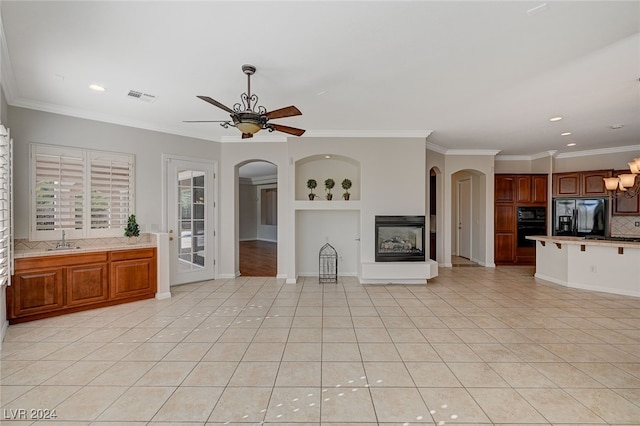 unfurnished living room with sink, crown molding, light tile patterned flooring, and ceiling fan with notable chandelier