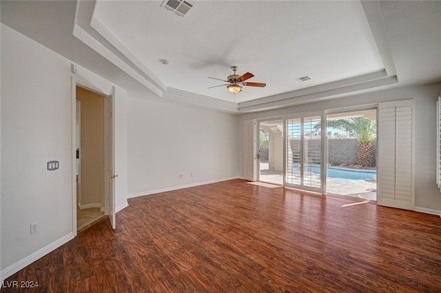 empty room with dark hardwood / wood-style floors, a tray ceiling, and ceiling fan