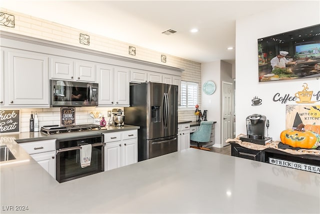 kitchen with appliances with stainless steel finishes, white cabinets, hardwood / wood-style floors, and backsplash