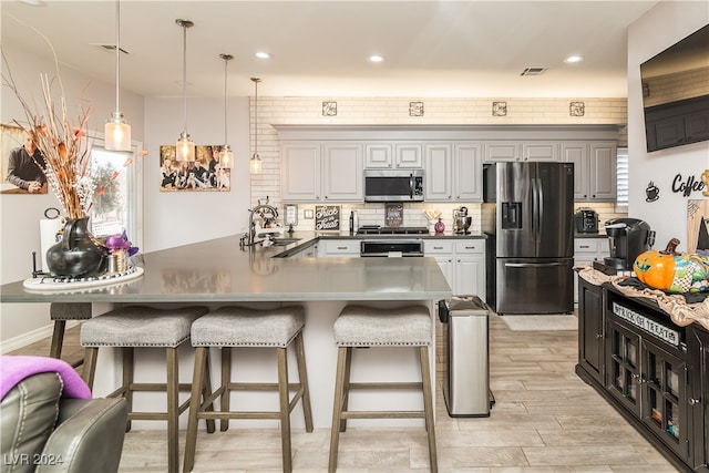 kitchen with a kitchen breakfast bar, light wood-type flooring, stainless steel appliances, sink, and decorative light fixtures