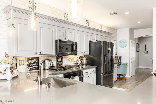 kitchen featuring sink, hardwood / wood-style floors, white cabinetry, hanging light fixtures, and stainless steel appliances