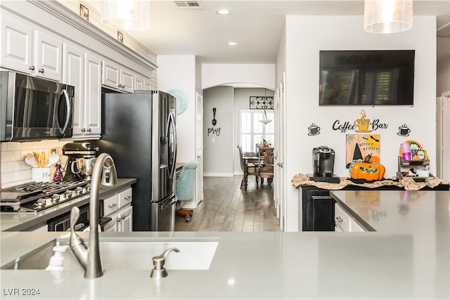 kitchen featuring wood-type flooring, stainless steel appliances, decorative light fixtures, white cabinets, and decorative backsplash