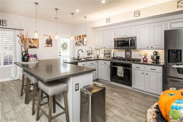 kitchen with a sink, appliances with stainless steel finishes, light wood finished floors, and dark countertops