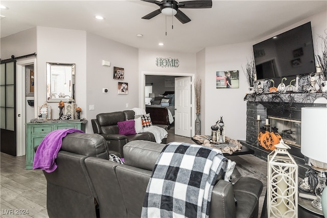 living room with a barn door, light hardwood / wood-style flooring, a fireplace, and ceiling fan