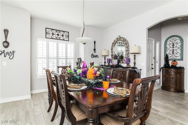 dining space featuring baseboards, arched walkways, and light wood finished floors