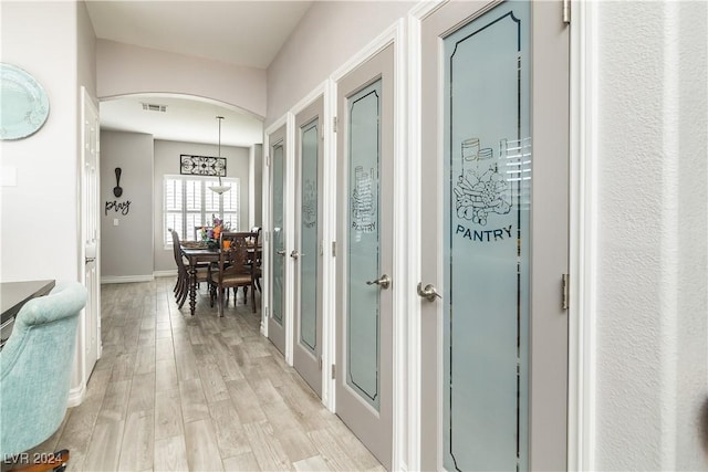 corridor featuring light wood-style floors, baseboards, arched walkways, and visible vents