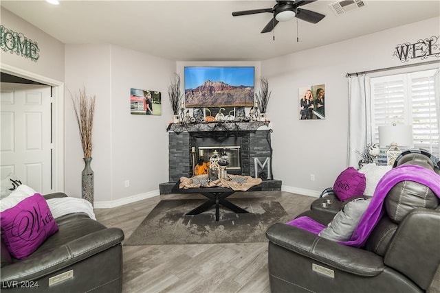 living room with ceiling fan, a stone fireplace, and wood-type flooring