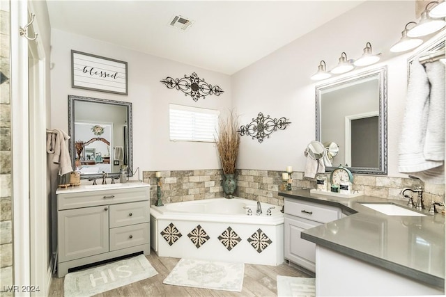 ensuite bathroom featuring visible vents, wood finished floors, a bath, two vanities, and a sink