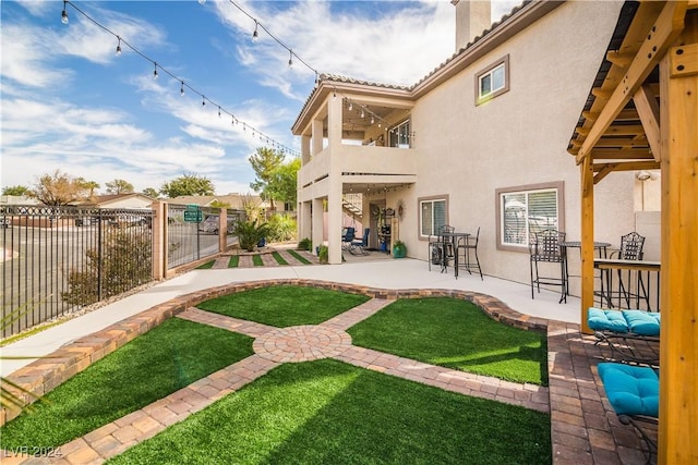 rear view of property with fence, a balcony, stucco siding, a chimney, and a patio area