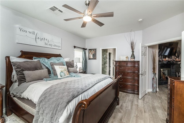 bedroom featuring a fireplace, light wood-style floors, a ceiling fan, ensuite bathroom, and visible vents