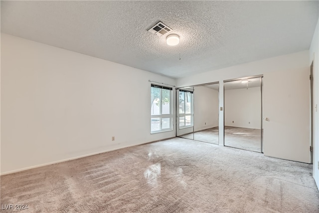 unfurnished bedroom featuring a textured ceiling, multiple closets, and carpet