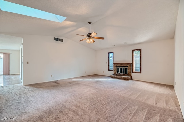 unfurnished living room with vaulted ceiling with skylight, light carpet, ceiling fan, and a brick fireplace