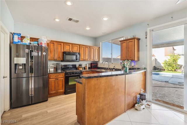 kitchen with light hardwood / wood-style flooring, kitchen peninsula, dark stone counters, sink, and black appliances