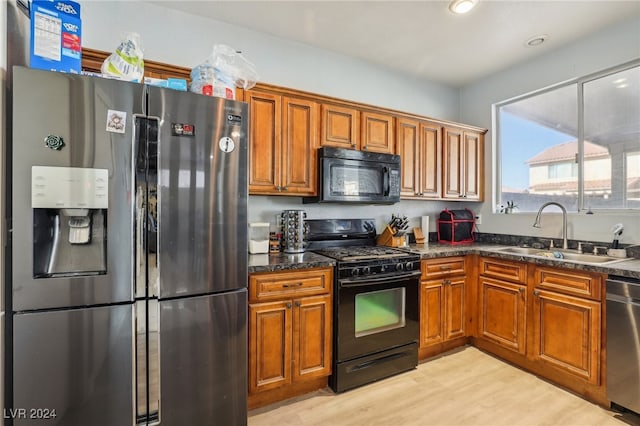 kitchen with dark stone countertops, light hardwood / wood-style floors, black appliances, and sink