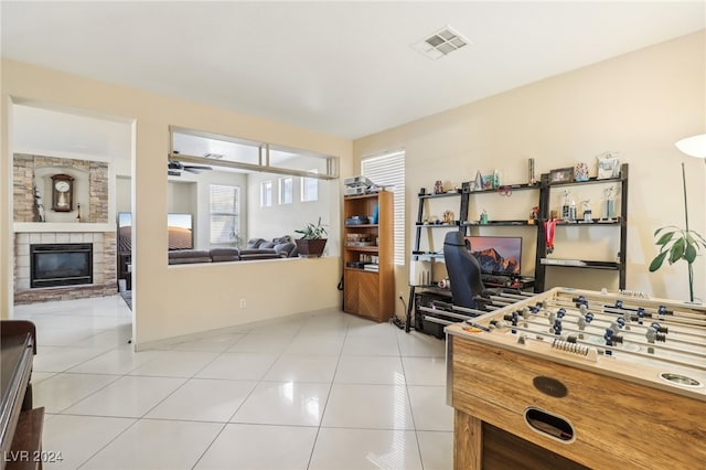 recreation room with light tile patterned flooring, a stone fireplace, and ceiling fan