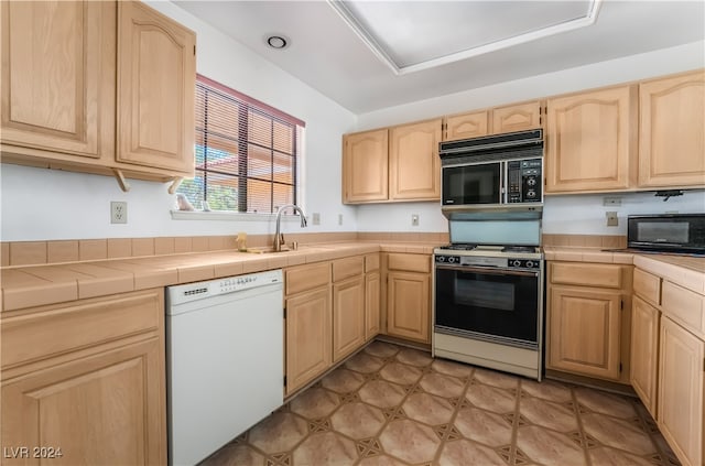 kitchen featuring tile countertops, dishwasher, light brown cabinets, and gas range oven