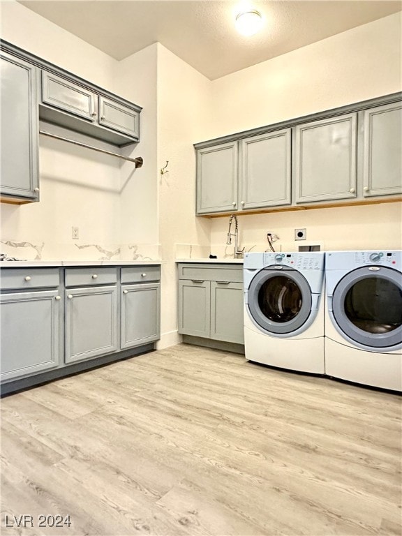 laundry room with washing machine and dryer, cabinets, and light wood-type flooring