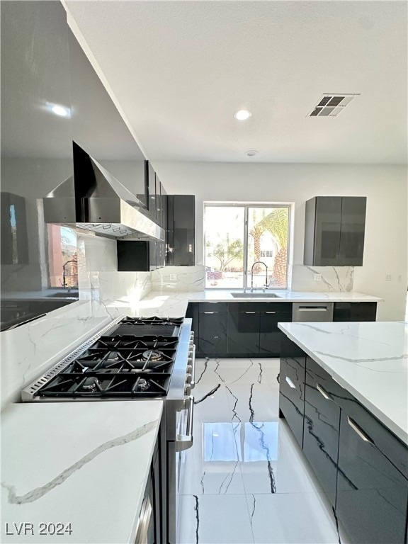 kitchen featuring wall chimney range hood, light stone counters, sink, and high end stainless steel range oven