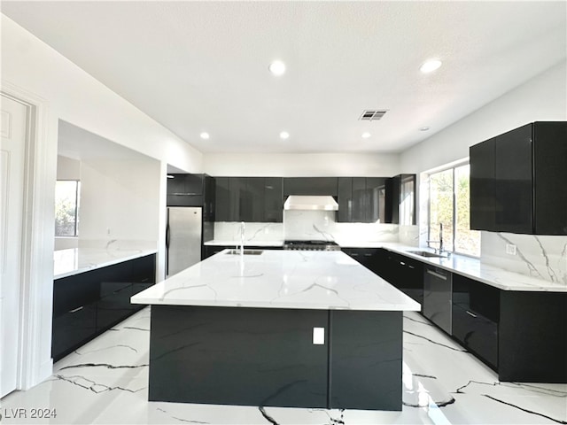 kitchen with a center island with sink, extractor fan, light stone countertops, sink, and stainless steel appliances