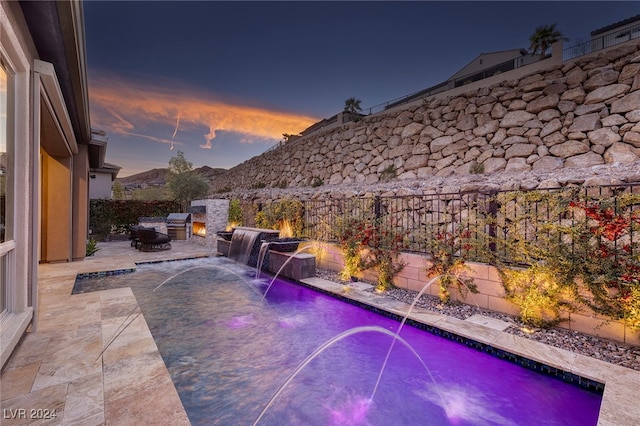 pool at dusk with a mountain view, pool water feature, and exterior kitchen