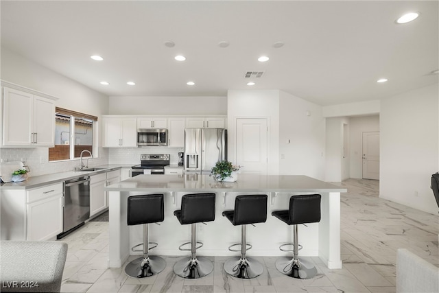 kitchen featuring appliances with stainless steel finishes, sink, a center island, white cabinets, and a breakfast bar