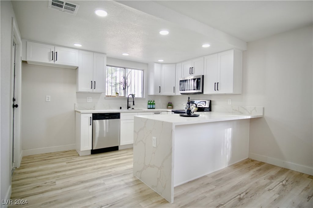 kitchen with white cabinetry, stainless steel appliances, light hardwood / wood-style flooring, and kitchen peninsula