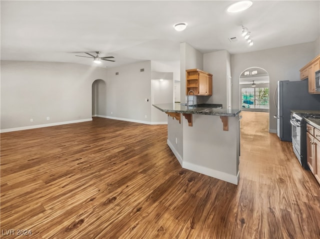 kitchen featuring a kitchen breakfast bar, ceiling fan, stainless steel appliances, dark stone countertops, and dark hardwood / wood-style floors