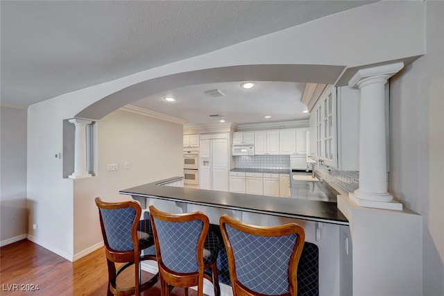 kitchen featuring kitchen peninsula, backsplash, white appliances, white cabinets, and light hardwood / wood-style floors