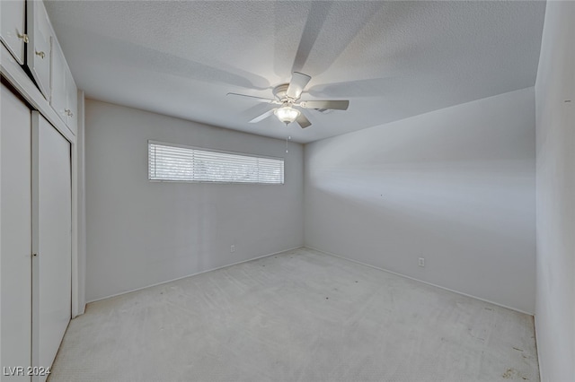 unfurnished bedroom with ceiling fan, a closet, light carpet, and a textured ceiling