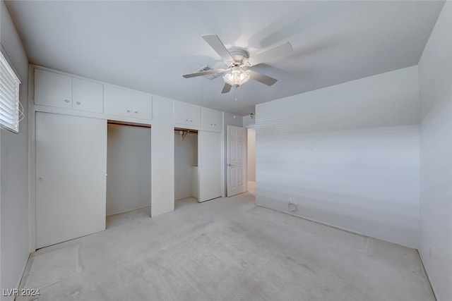 unfurnished bedroom featuring ceiling fan, light colored carpet, and two closets