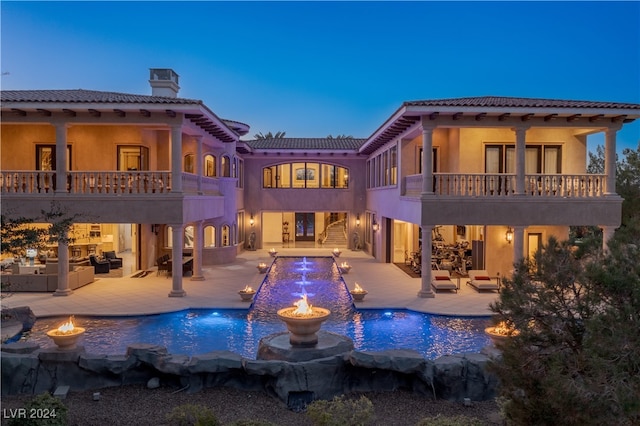 back house at dusk with a patio area, pool water feature, a balcony, and an outdoor hangout area