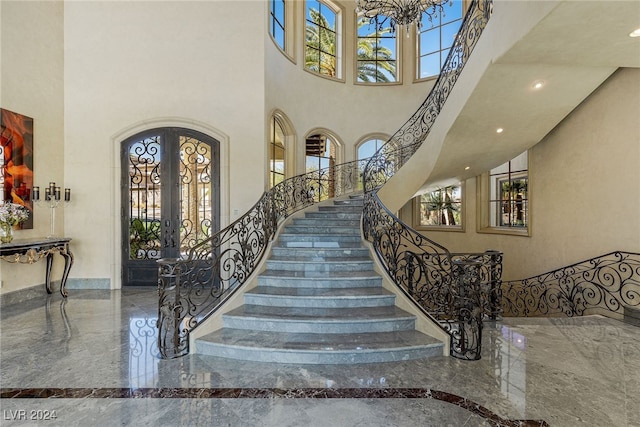 stairway featuring a towering ceiling, french doors, an inviting chandelier, and plenty of natural light