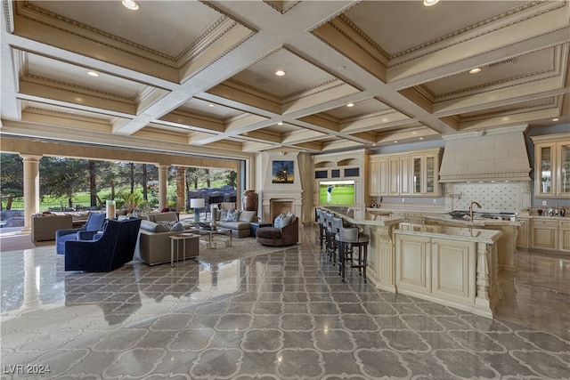 interior space featuring coffered ceiling, cream cabinets, a kitchen breakfast bar, an island with sink, and custom range hood