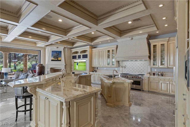 kitchen with a center island with sink, custom exhaust hood, range with two ovens, and cream cabinets