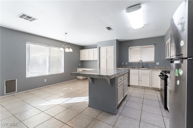 kitchen with black range, a breakfast bar area, a kitchen island, hanging light fixtures, and stainless steel refrigerator