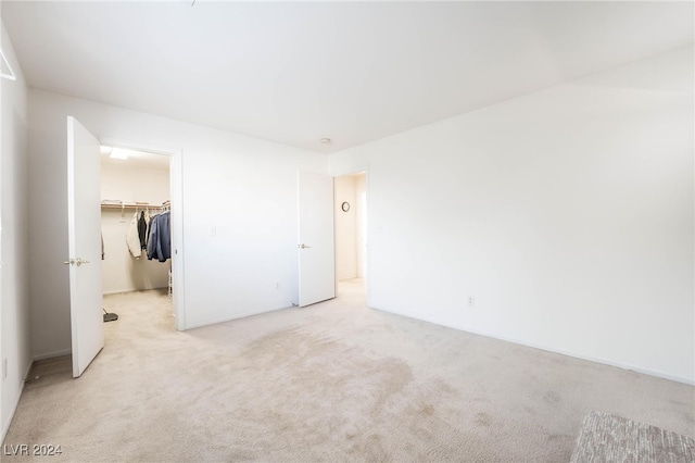 unfurnished bedroom with a closet, light carpet, and a walk in closet