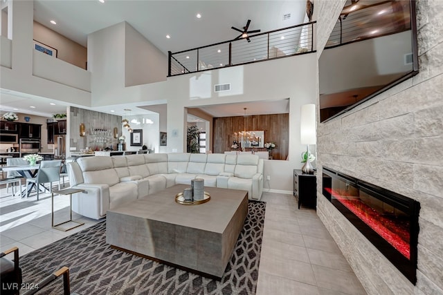 tiled living room featuring a towering ceiling, a tile fireplace, and ceiling fan with notable chandelier