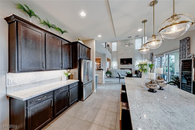 kitchen with high end refrigerator, light stone countertops, a stone fireplace, dark brown cabinets, and hanging light fixtures